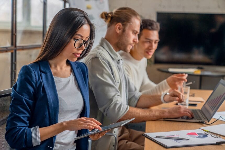 Asian female working on digital tablet. Young businessman in meeting with coworkers Importanța digitalizării în lumea modernă