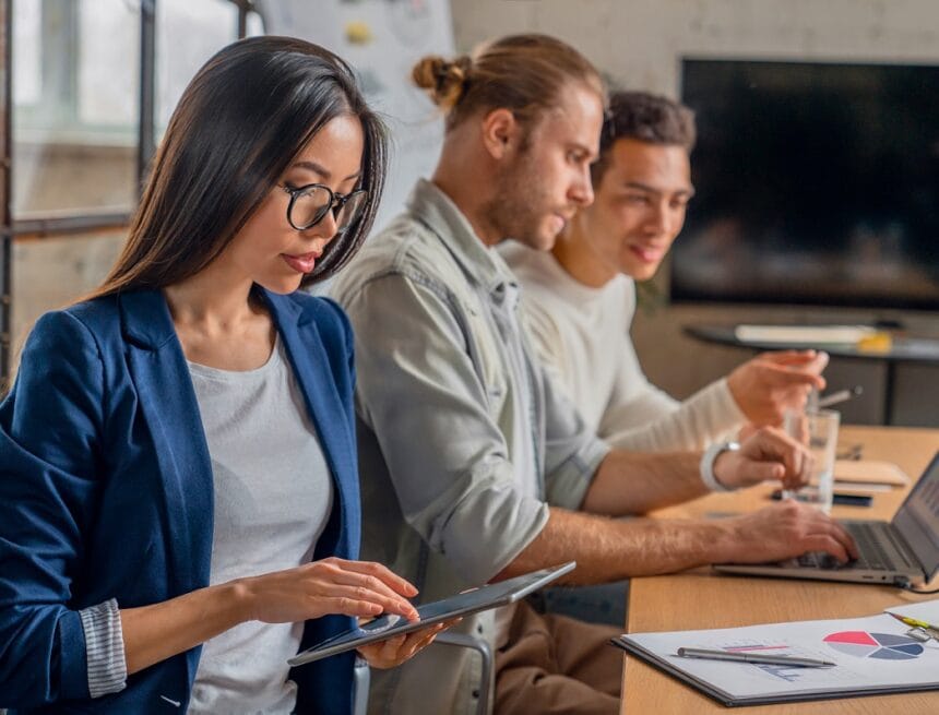 Asian female working on digital tablet. Young businessman in meeting with coworkers Importanța digitalizării în lumea modernă