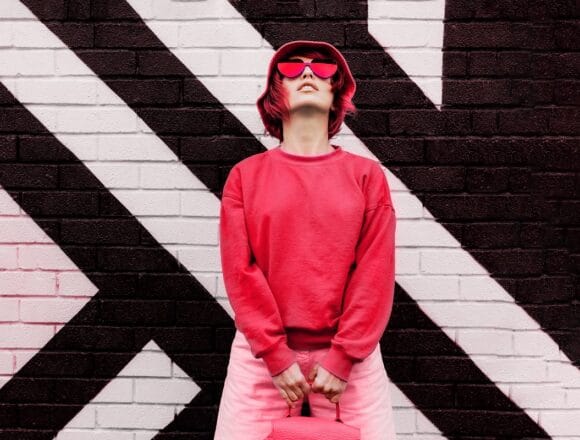 Hipster fashion young woman in trendy magenta color sweatshirt and sunglasses and bucket hat posing on the painted brick wall background. Color of the 2023 year. Urban city street fashion. Tendințele în moda pentru femei în 2023: Cele mai apreciate ținute și stiluri de îmbrăcăminte