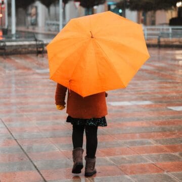 Copil cu umbrelă portocalie pe o stradă udă de ploaie, toamna