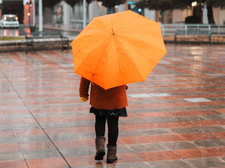 Copil cu umbrelă portocalie pe o stradă udă de ploaie, toamna Copil cu umbrelă portocalie pe o stradă udă de ploaie, toamna