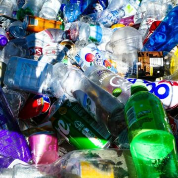 Grămadă de sticle PET și doze de băuturi pregătite pentru returnare și reciclare